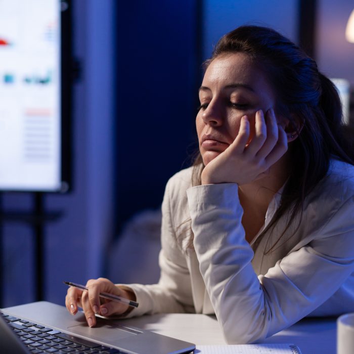 Tired remote woman talking nap on chair working on laptop, analysing financial statistics in company office. Busy woman using modern technology network wireless late at night